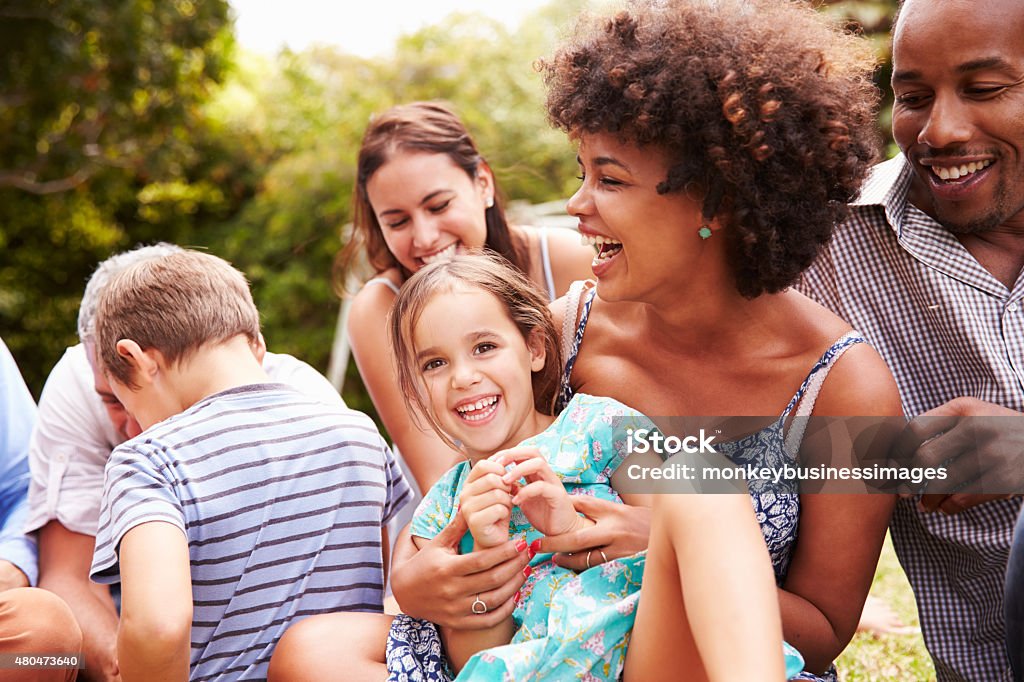 Adults and kids sitting on the grass in a garden Multiracial Group Stock Photo