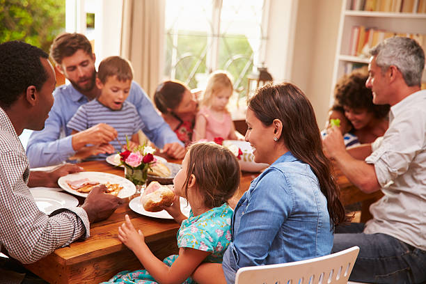 família e amigos sentado em uma mesa de jantar - eating people group of people home interior imagens e fotografias de stock