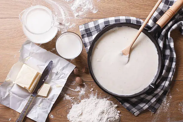 Preparation of bechamel sauce in a pan and ingredients on the table. horizontal view from above