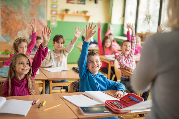 school children raising their hands ready to answer the question. - basisschool stockfoto's en -beelden