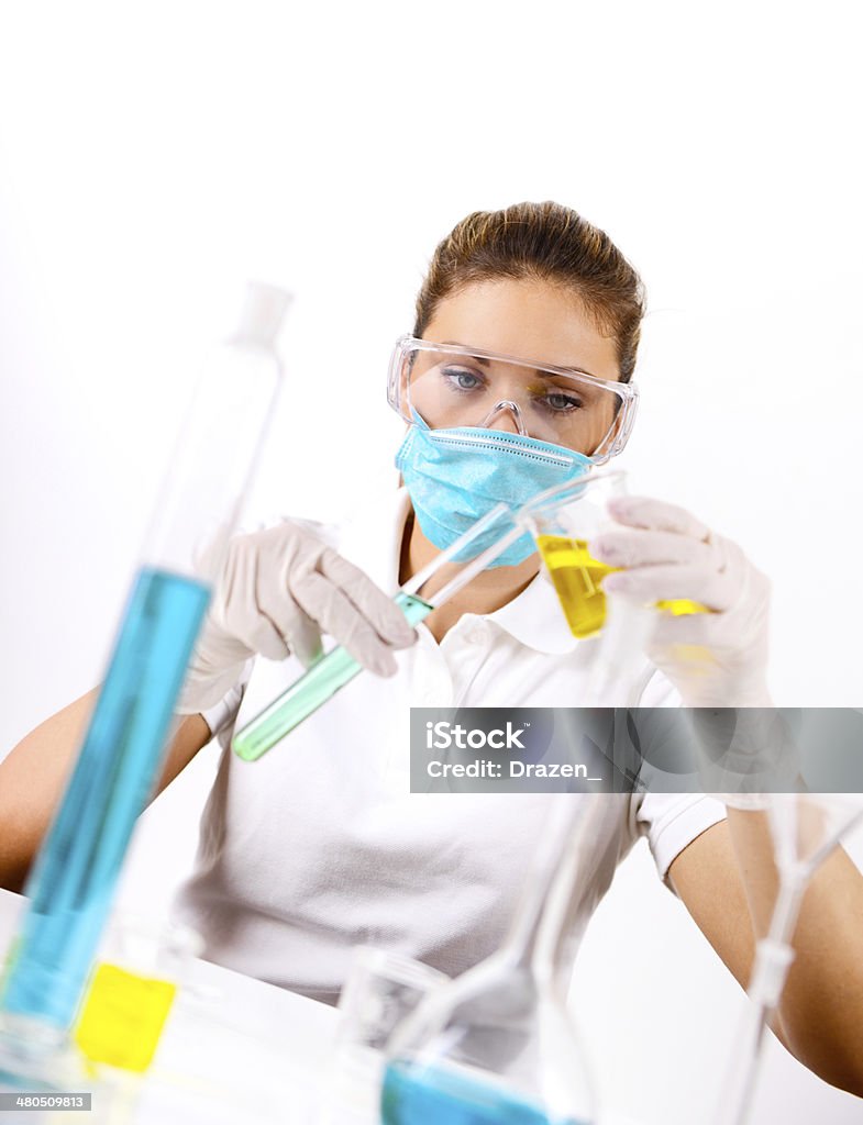 Young pharmaceutical PhD scientist experimenting in laboratory with chemical solutions Researcher in the lab, examining solutions in test tubes. Woman wearing protective gloves and mask Adult Stock Photo