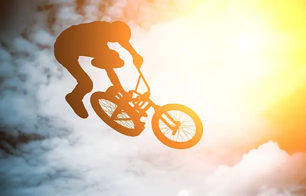 Silhouette of a man doing an jump with a bmx bike against sunshine sky.