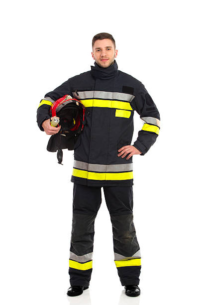 feuerwehrmann posieren mit helm unter dem arm - isolated on white full length red protection stock-fotos und bilder