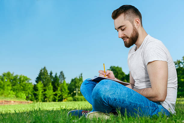 istock Young man sitting on the grass in park with diary 480543190