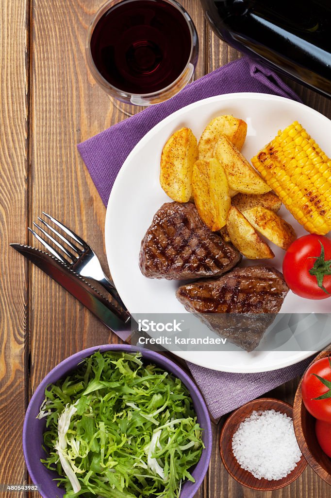 Steak with grilled potato, corn, salad and red wine Steak with grilled potato, corn, salad and red wine on wooden table. Top view 2015 Stock Photo