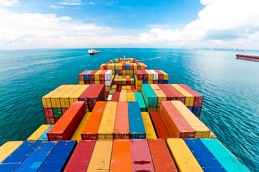 Horizontal wide angle view of heavy loaded container cargo ship in busy strait of Malacca.