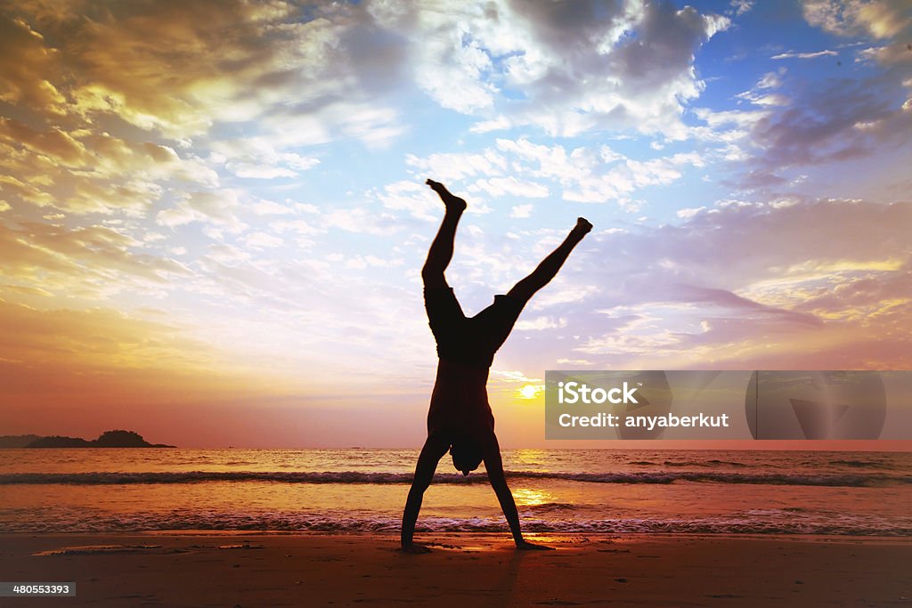 Mann macht handstand am Strand bei Sonnenuntergang - Lizenzfrei Freude Stock-Foto