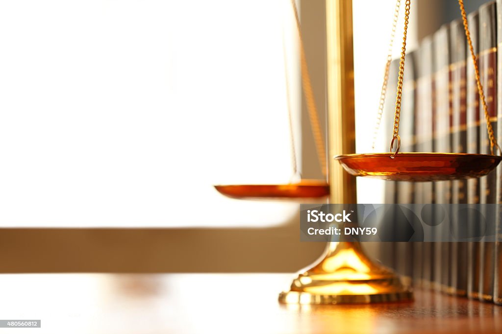 Justice Scale Next To Row Of Law Books A justice scale on a desk next to a row of law books. Light filters in through a window in the background creating ample negative space for coy.  Photographed using a very shallow depth of field. Equal-Arm Balance Stock Photo