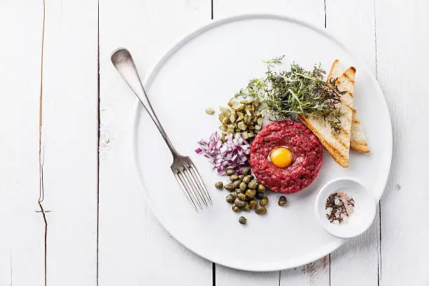 Beef tartare with capers and onion on white wooden background