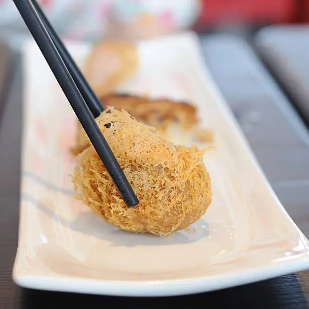 Black chopsticks catch Chinese fried-food on white plate.