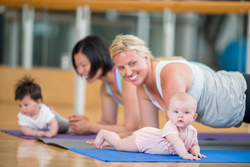 Mothers and their babies staying active and healthy by doing exercises (yoga, stretching, and aerobics) together at a health club.