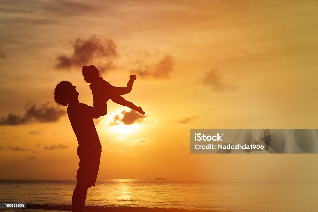 Father and little daughter silhouettes at sunset Father and little daughter silhouettes on beach at sunset 2015 Stock Photo