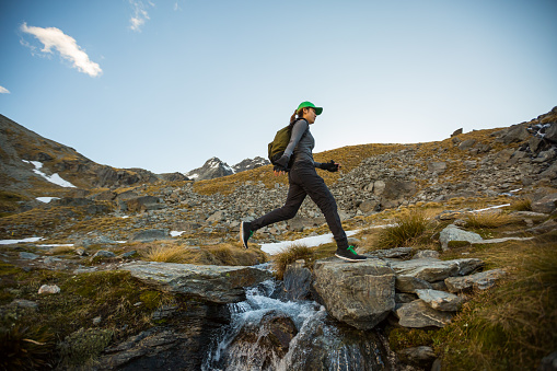 Female hiker with backpack leaping across a stream. New Zealand