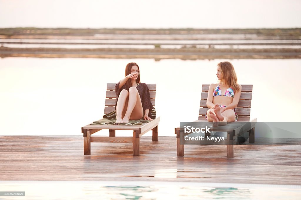 Two Young Women relaxing at the Swimming Pool Two young female friends sunbathing and talking at the outside swimming pool. Sečovlje, Portorož, Slovenia.  Outdoors Stock Photo