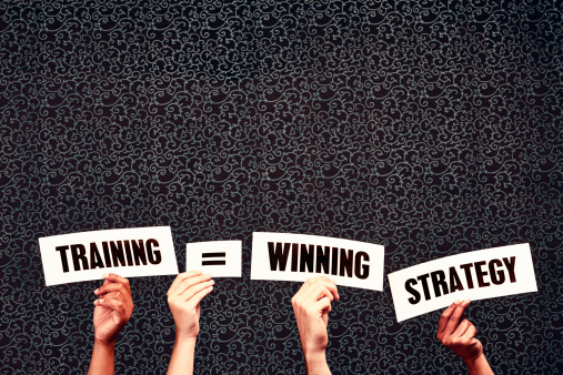 Three hands hold up words saying 'Training = Winning Strategy' against a dark background. The more trainng you get, the better you and your company are likely to do! Lots of copy space on the dark background above the words for your message.