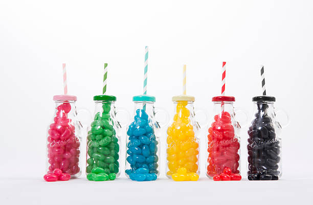 Colored Jelly Beans in Bottles Different colored Jelly Beans in separate glass jars with straws, set against a white background. red bean dessert stock pictures, royalty-free photos & images