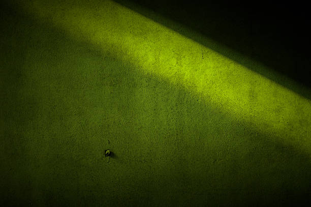 Grungy green wall background partly illuminated by a slanting ray of sunlight. Toned, dark composite image.