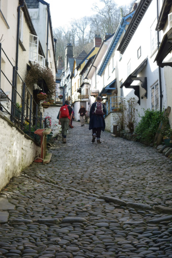 Clovelly,UK - February 10, 2014: Walkers climb the cobbled Clovelly street.  One of the sedges used to deliver goods is proppedup alongside a wall.