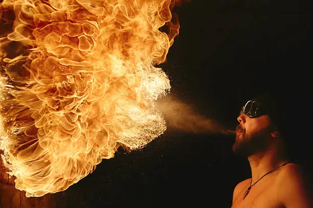 Fire breather blowing a fire ball from his mouth.