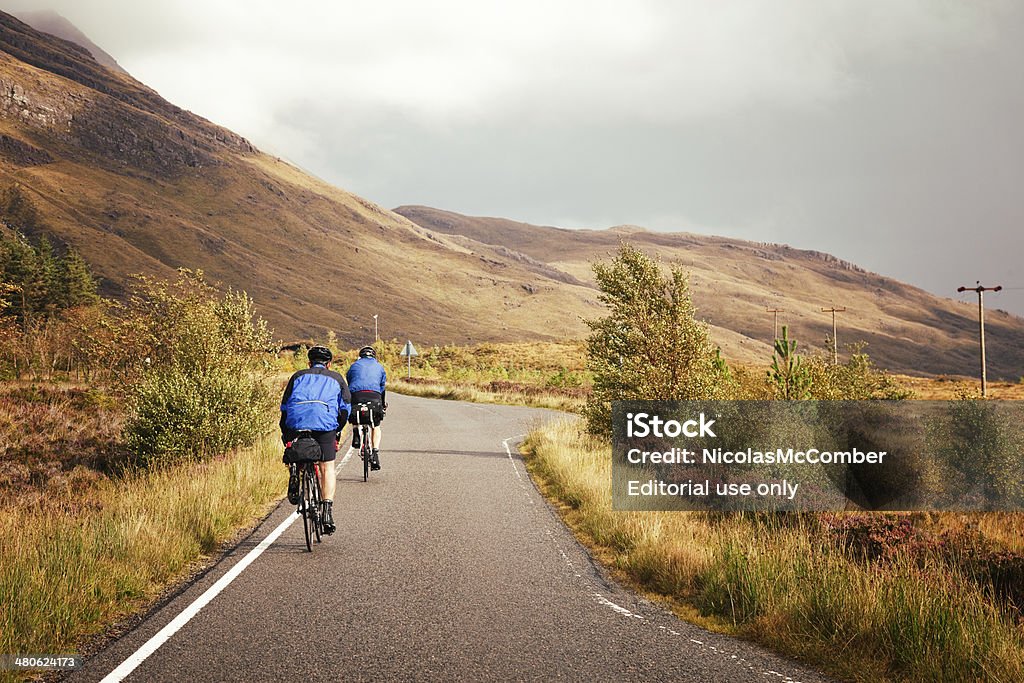 Cycling through the Highlands Ardelve, UK - September 24, 2011: Two cyclists ride their bikes on a small back road through Scotland's Wester Ross. Cycling Stock Photo