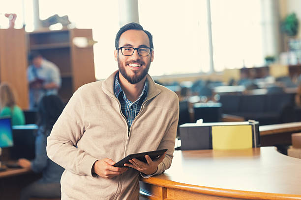 Trendy adult college student in library with digital tablet