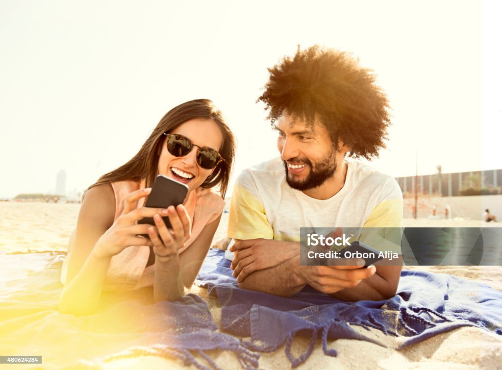 Young couple lying on blanket on beach, using smart phone Beach Stock Photo