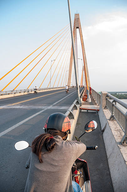 My Tho, Vietnam - March 25, 2012: A young woman about to ride her motorcycle over Cau Rach Mieu suspension bridge in My Tho, Vietnam
