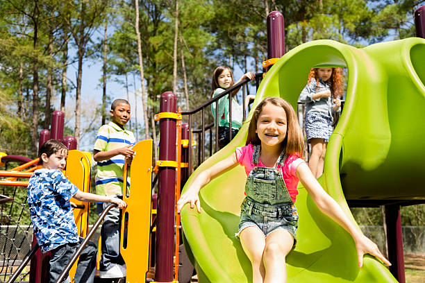 Elementary children play at school recess or park on playground. Five elementary-age children play during school recess or at a park setting. Playground equipment, slide.  playground stock pictures, royalty-free photos & images