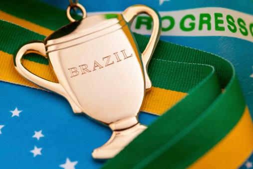 Brazil will host the 2014 World Cup Tournament. Brazil have won the tournament, that takes place every 4 years, on 5 occasions.  A Gold Cup medal engraved with Brazil text and a yellow and green ribbon on a Brazilian flag background.