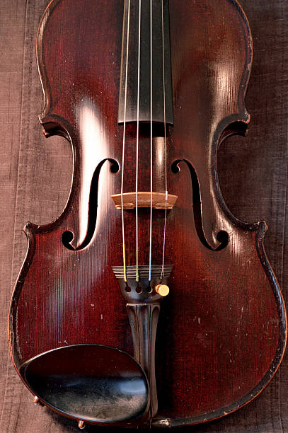 Antique violin against gray background Old violin against gray seamed fabric. Violin is an antique from the early 1800's in a dark stain (original finish). violin f hole stock pictures, royalty-free photos & images
