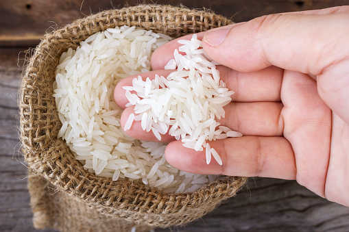 Woman's hand picking uncooked rice in a small  burlap sack. On wooden background. Top view.