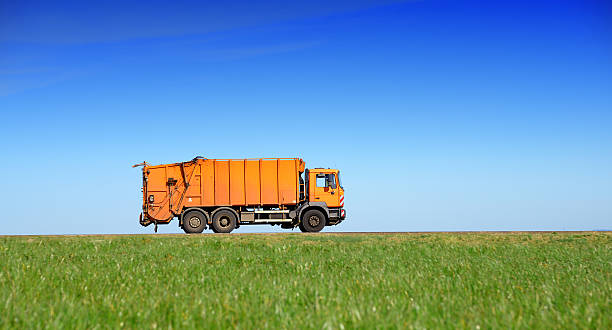 Garbage truck drives on country road through fields stock photo