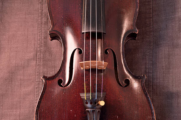 Antique violin against gray fabric background Old violin against gray seamed fabric. Violin is an antique from the early 1800's in a dark stain (original finish). violin f hole stock pictures, royalty-free photos & images