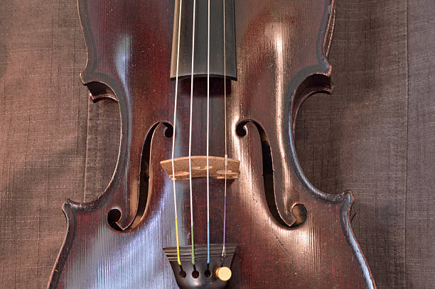 Antique violin closeup against gray fabric background Old violin against gray seamed fabric. Violin is an antique from the early 1800's in a dark stain (original finish). violin f hole stock pictures, royalty-free photos & images