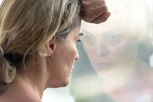 Pensive hispanic mature woman looking through a window