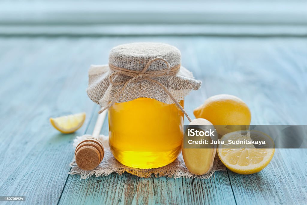 honey in jar with twine, honey dipper, lemon and ginger Natural honey in a pot or jar with twine tied in a bow, honey dipper, lemon and ginger on a blue wooden background 2015 Stock Photo