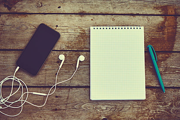 Bank notebook with pencil laying on the brown table. Vintage old tape player with headphones put on the table as well.