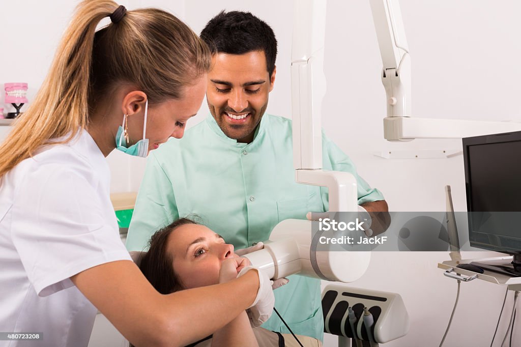 Dentist examines patient at clinic Smiling dentist with assistant examines patient's oral cavity on apparatus for xray 20-29 Years Stock Photo
