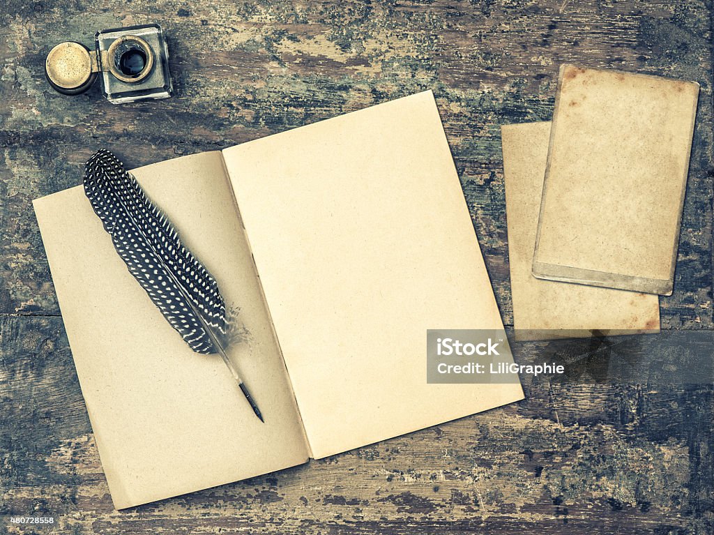 Open book, antique writing tools feather pen and inkwell. Open book, antique writing tools feather pen and inkwell on textured wooden background. Vintage style toned picture Book Stock Photo