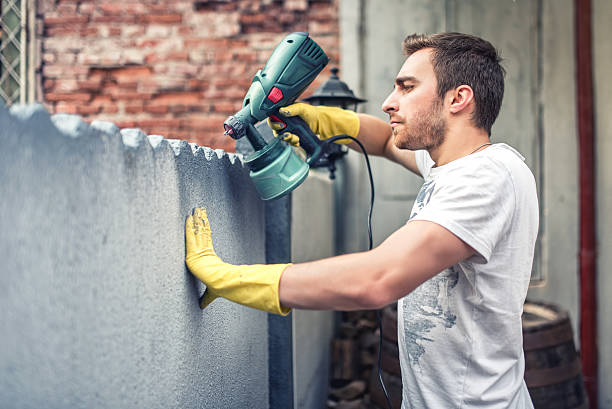 Man using gloves painting grey wall with spray paint gun
