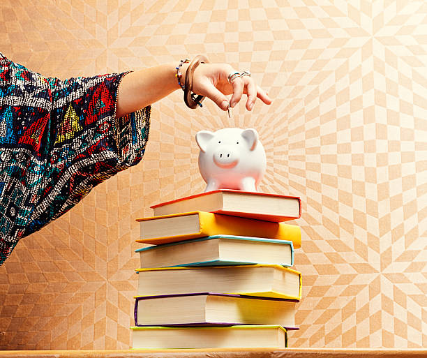 istock Female hand adds coin to piggybank on book stack 480739345