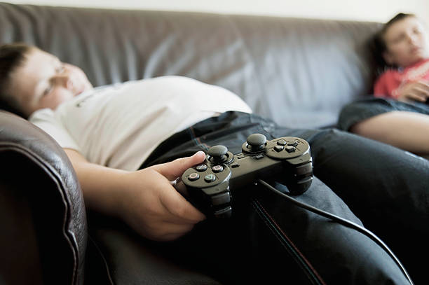 Boys Sleeping On Sofa While Holding Games Consoles stock photo