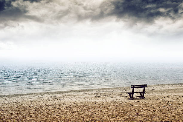 Empty wooden bench on the beach in cloudy weather. Concept of loneliness, emptiness, solitude.