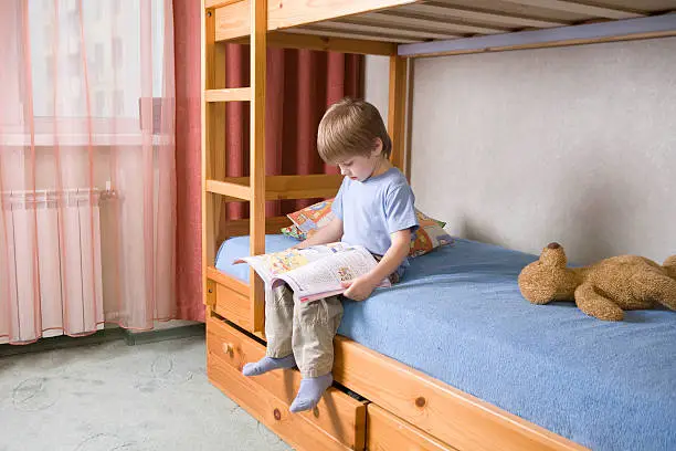 Full length of young boy reading book on bunk bed