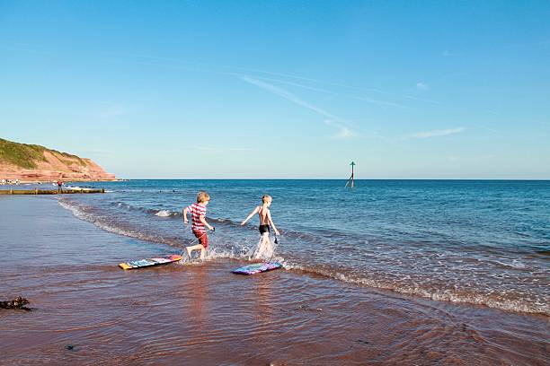 Braving the sea Two boys pulling their body boards into the sea exmouth western australia stock pictures, royalty-free photos & images