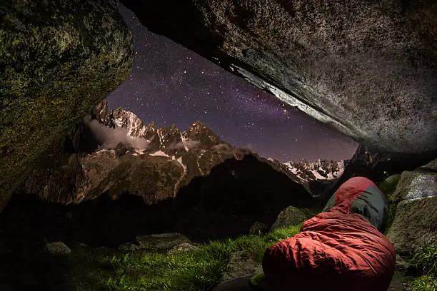 Alpine bivuac, sleeping bag with Charpua Glaciar bassin Aguille Verte lit by moonlight milky way Mont Blanc Massif, France