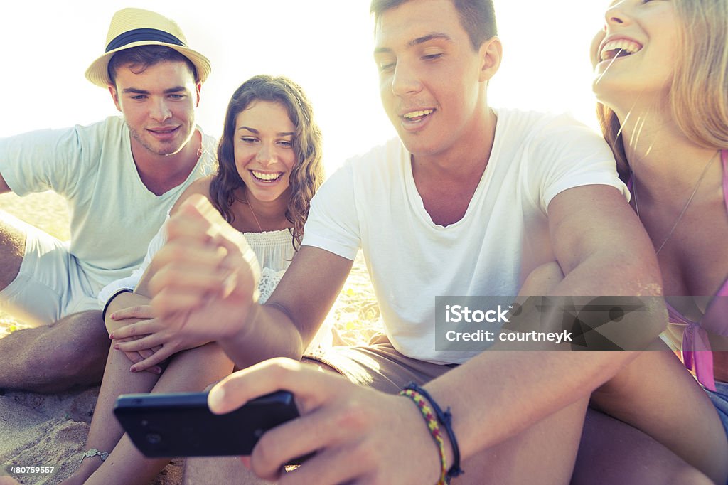 Friends at the beach looking at mobile phone Friends at the beach looking at mobile phone. Close upFriends at the beach looking at mobile phone with beer 20-29 Years Stock Photo