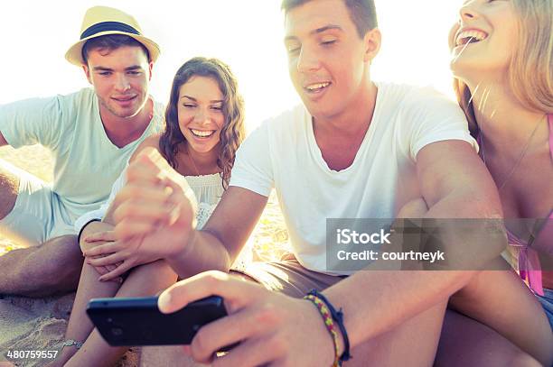 Friends At The Beach Looking At Mobile Phone Stock Photo - Download Image Now - 20-29 Years, Adult, Adults Only