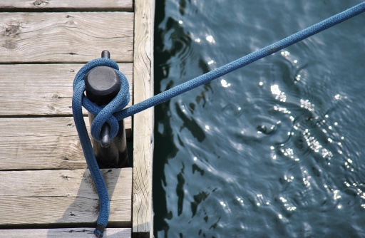 A close-up depiction of mooring, blue rope attached to a black metal bollard on a wooden pier.