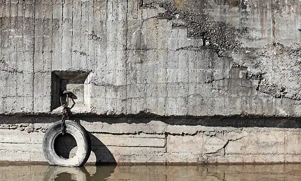 Photo of Old concrete mooring wall with automotive tire